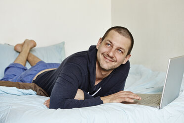 Mittlerer erwachsener Mann auf dem Bett liegend mit Laptop - ISF15266