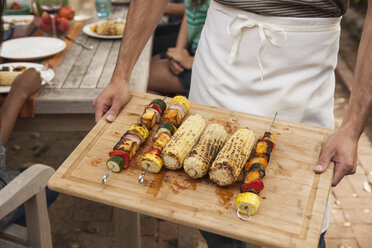 Man holding tray of barbecued vegetable skewers and corn on the cob - ISF15277