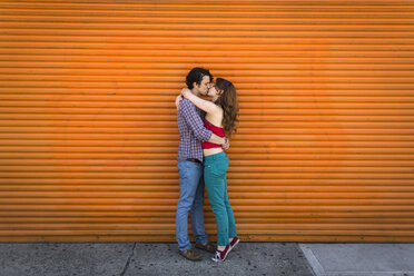 Romantisches Paar, das sich vor einem orangefarbenen Fensterladen küsst - ISF15292