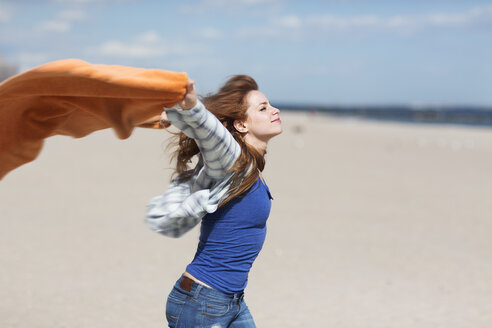 Young woman holding up blanket on windy beach - ISF15299