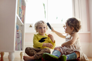 Weibliches Kleinkind bürstet männlichen Kleinkindern die Haare im Spielzimmer - ISF15314