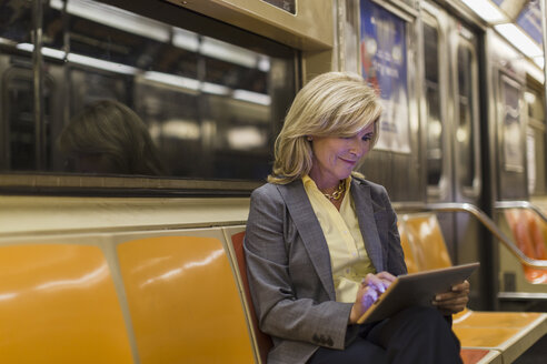 Ältere Frau sitzt in der U-Bahn und benutzt ein digitales Tablet - ISF15340