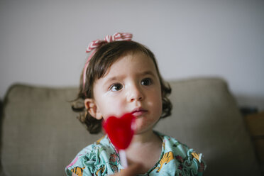 Niedliches kleines Mädchen isst einen herzförmigen Lutscher zu Hause - GEMF02105
