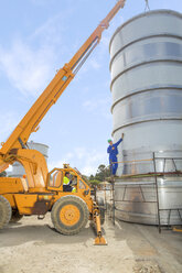 Construction worker in crane talking to co-worker at tank on construction site - ZEF15747