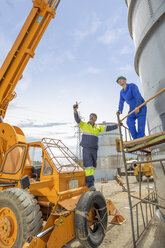 Bauarbeiter auf einem Kran im Gespräch mit einem Kollegen an einem Tank auf der Baustelle - ZEF15748