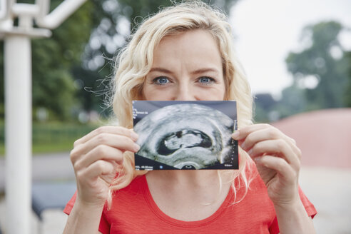 Porträt einer glücklichen schwangeren Frau, die ein Ultraschallbild im Freien hält - RHF02045