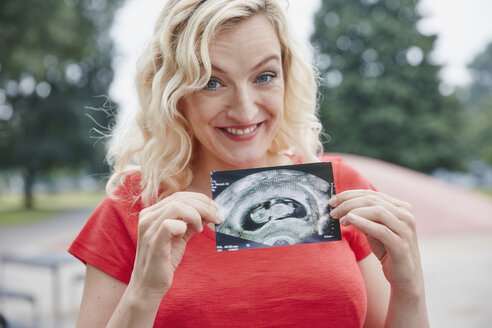 Porträt einer glücklichen schwangeren Frau, die ein Ultraschallbild im Freien hält - RHF02049
