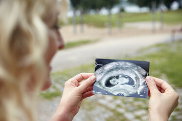 Pregnant woman looking at ultrasound image outdoors - RHF02050