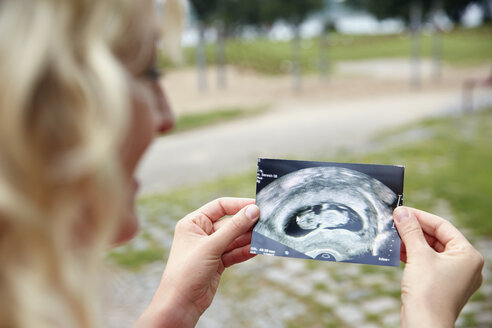 Schwangere Frau betrachtet Ultraschallbild im Freien - RHF02050