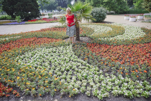 Pregnant woman standing amidst blooming flowers in park - RHF02052