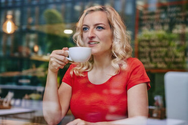 Porträt einer lächelnden blonden Frau, die in einem Café Kaffee trinkt - RHF02071
