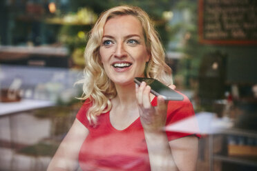 Portrait of happy blond woman using smartphone in a cafe - RHF02073