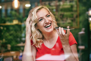 Portrait of laughing blond woman using smartphone in a cafe - RHF02074