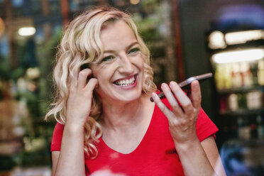 Porträt einer glücklichen blonden Frau mit Smartphone in einem Café - RHF02076