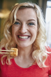 Porträt einer glücklichen blonden Frau, die Tofu isst - RHF02083