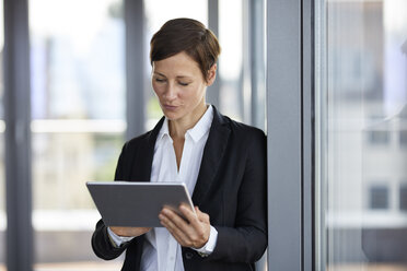 Businesswoman using tablet at the window in office - RBF06360