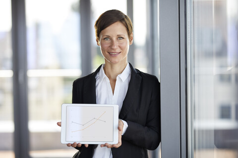 Portrait of smiling businesswoman in office holding tablet showing ascending line graph stock photo