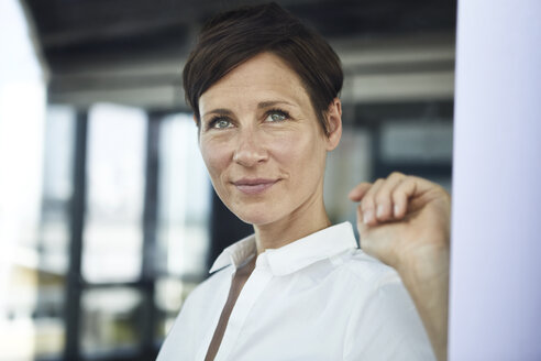 Portrait of smiling businesswoman in office looking out of window - RBF06372