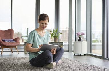 Woman sitting on the floor at home using tablet - RBF06389