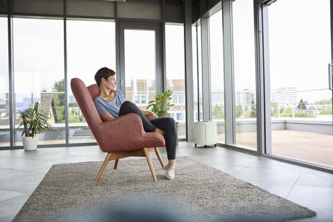 Frau sitzt im Sessel zu Hause und schaut aus der Balkontür, lizenzfreies Stockfoto