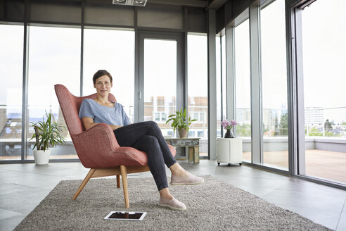 Portrait of woman sitting in armchair at home with tablet beside her - RBF06394