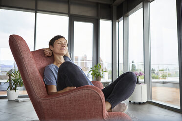 Woman sitting in armchair at home relaxing with closed eyes - RBF06397