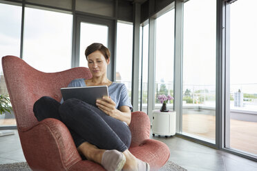 Frau sitzt in einem Sessel zu Hause und benutzt ein Tablet - RBF06398