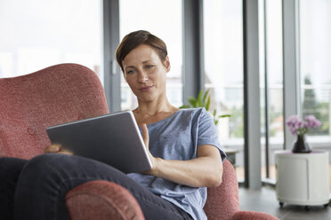 Frau sitzt in einem Sessel zu Hause und benutzt ein Tablet - RBF06401