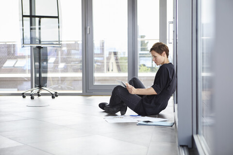 Geschäftsfrau sitzt auf dem Boden im Büro und benutzt ein Tablet, lizenzfreies Stockfoto