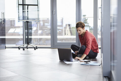 Geschäftsfrau sitzt auf dem Boden im Büro und benutzt einen Laptop - RBF06404