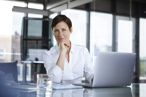 Porträt einer selbstbewussten Geschäftsfrau, die mit einem Laptop an einem Glastisch im Büro sitzt - RBF06408