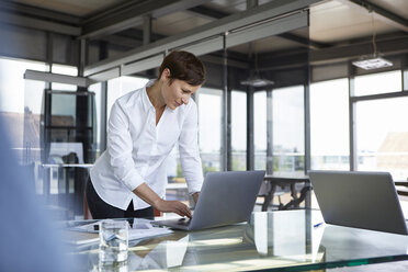 Geschäftsfrau steht an einem Glastisch im Büro und benutzt einen Laptop - RBF06411