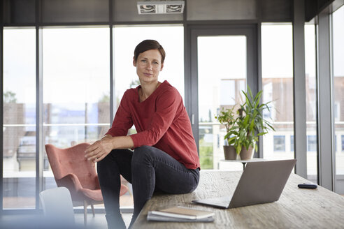 Porträt einer selbstbewussten Frau, die zu Hause mit einem Laptop auf einem Tisch sitzt - RBF06422