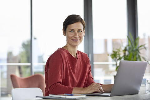 Portrait of smiling woman sitting at table at home using laptop stock photo