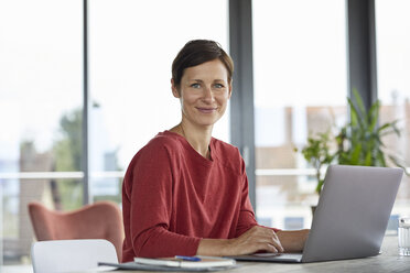 Portrait of smiling woman sitting at table at home using laptop - RBF06423