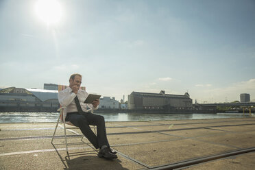 Businessman sitting on chair on tram tracks using tablet - CUF38091