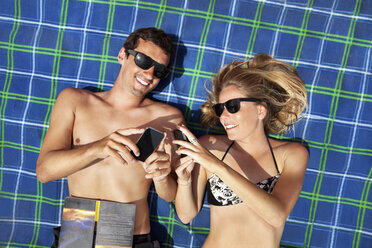 Junges Paar liegt auf einem Strandtuch und benutzt Smartphones - CUF38095