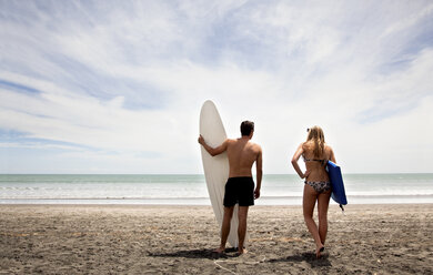 Junges Paar steht am Strand und hält Surfbrett und Boogie Board - CUF38096