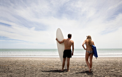 Young couple standing on beach holding surfboard and boogie board - CUF38096