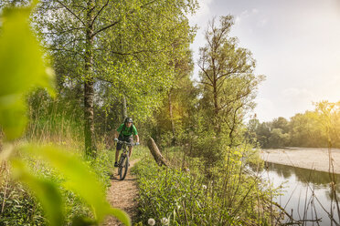 Junger Mann auf dem Fahrrad entlang des Flussufers - CUF38097