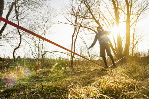 Junger Mann balanciert auf einem Bein auf einer Slackline in einer Feldlandschaft - CUF38101