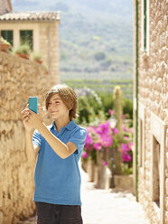 Boy taking selfie on smartphone on village street, Majorca, Spain - CUF38109