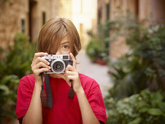 Portrait of boy photographing village street using SLR camera, Majorca, Spain - CUF38112