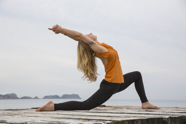 Mittlere erwachsene Frau, die sich nach hinten beugt und Yoga auf einer hölzernen Seebrücke praktiziert - CUF38113