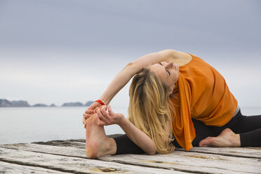 Mid adult woman touching toes practicing yoga on wooden sea pier - CUF38114