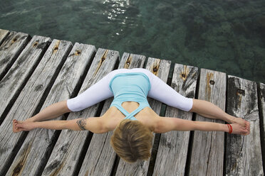 Draufsicht auf eine erwachsene Frau mit ausgestreckten Armen und Beinen, die auf einer hölzernen Seebrücke Yoga übt - CUF38115