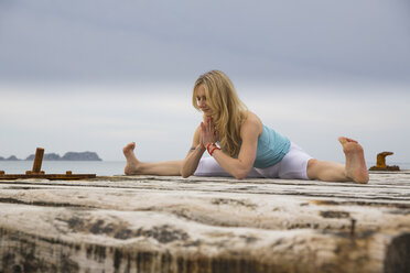 Mid adult woman with hands together practicing yoga on wooden sea pier - CUF38116
