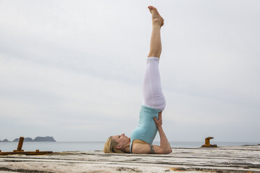 Mittlere erwachsene Frau mit hochgelegten Beinen, die Yoga auf einer hölzernen Seebrücke praktiziert - CUF38118