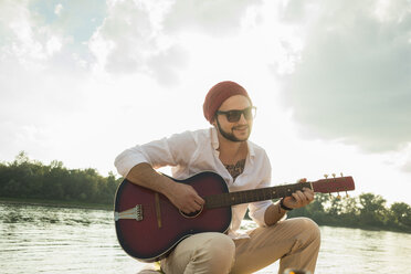 Young man sitting by lake playing guitar - CUF38135