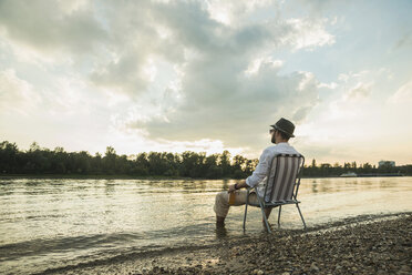 The boy is sitting on a folding chair on the shore of a lake or river.  Recreation, weekends, tourism. Rear view - a Royalty Free Stock Photo from  Photocase